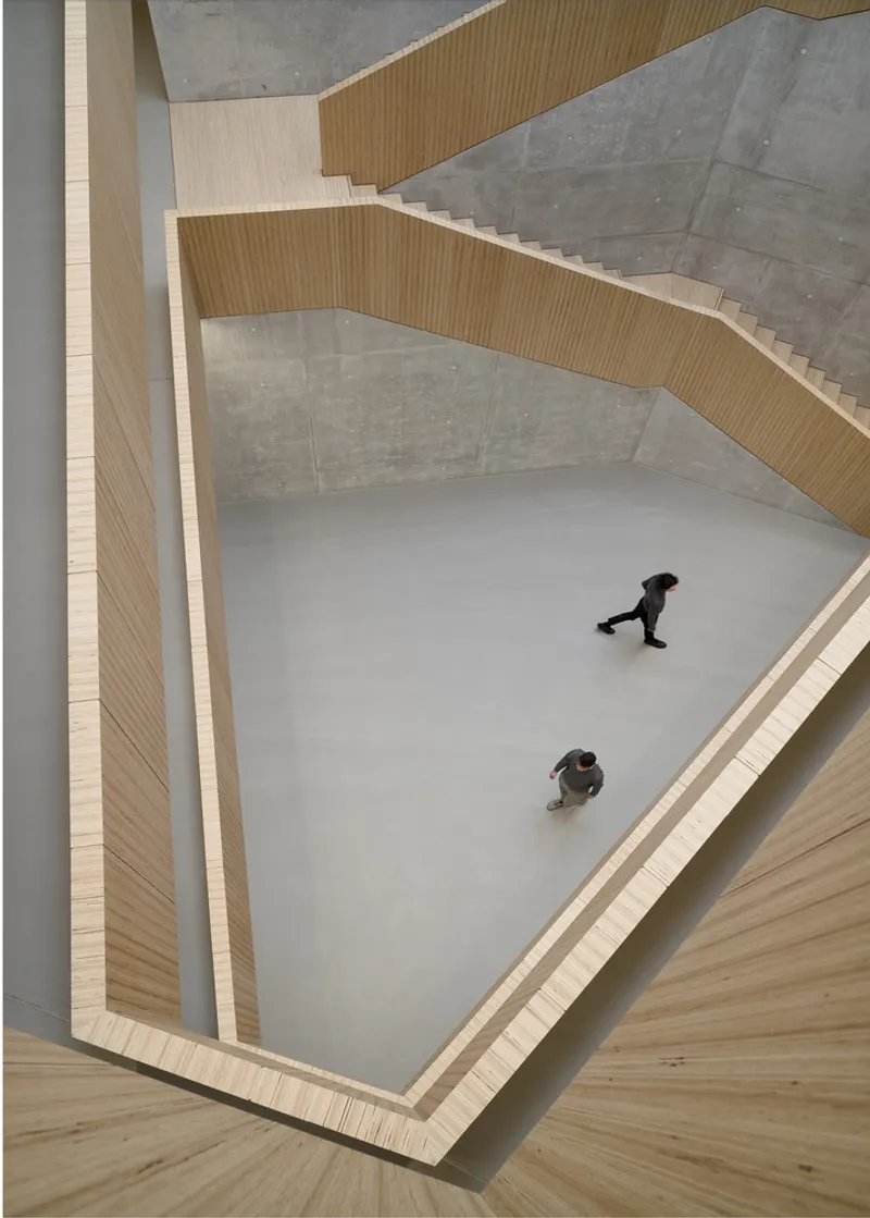 Top-down view into the curved atrium with two figures walking across the polished floor