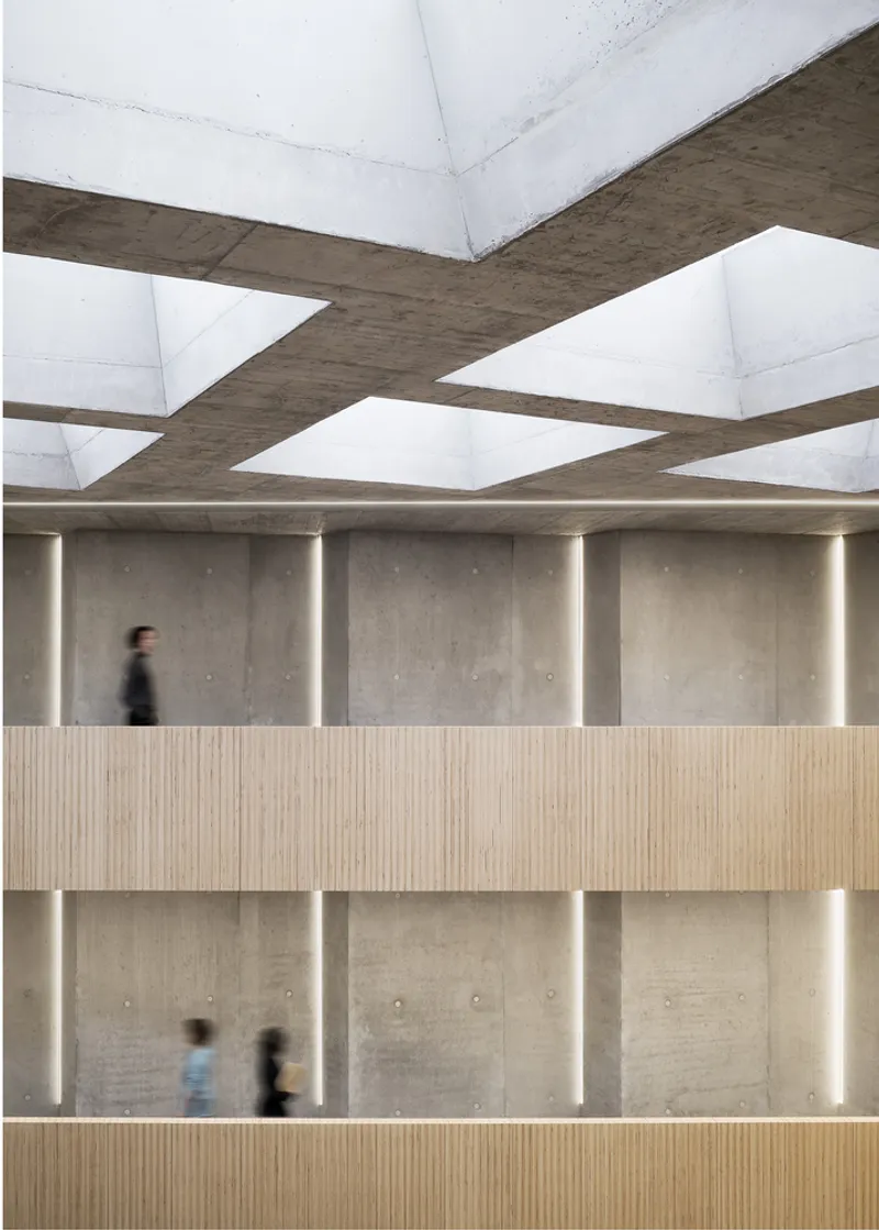 Interior atrium with timber-clad balconies, concrete walls with vertical lighting slots, and pedestrians crossing below