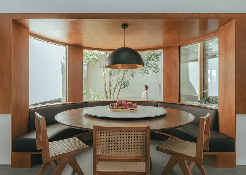 Curved timber breakfast nook with built-in banquette seating and windows overlooking the planted courtyard