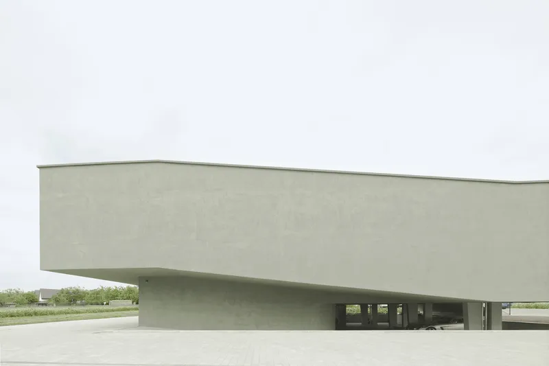 Cantilevered concrete volume hovering above the paved plaza on an overcast day
