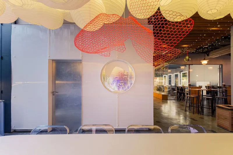White partition wall with circular porthole window beneath red mesh fish sculpture suspended from ceiling