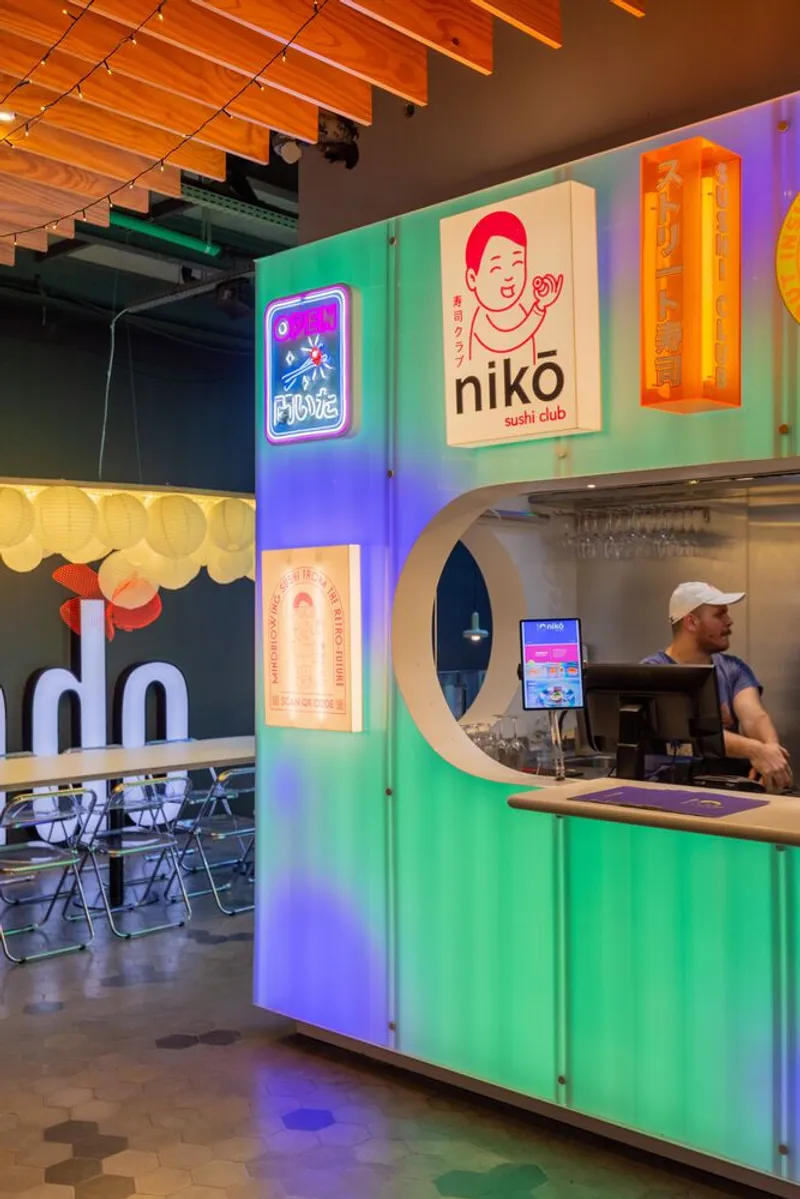 Food kiosk with corrugated metal cladding, illuminated signage panels, and circular service window under exposed timber ceiling