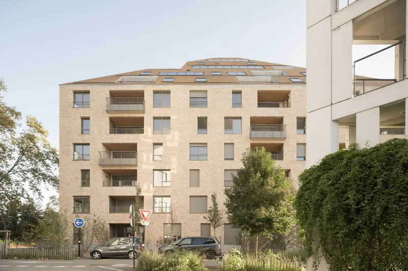 Street view of the rounded brick tower with layered balconies and parked cars at its base