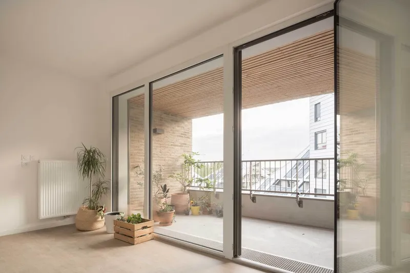 Interior room with sliding glass doors opening onto a balcony with potted plants and metal railing