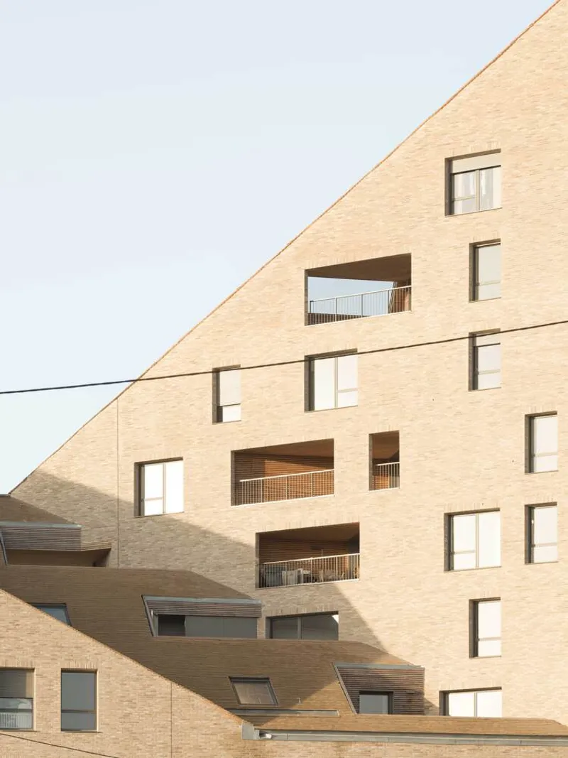 Close-up of the angled brick facade showing punched window openings and recessed balconies with railings