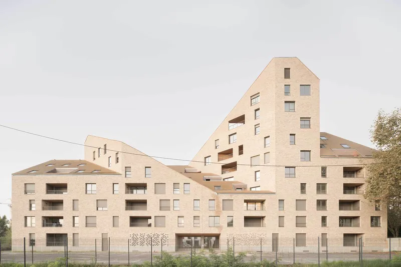 Pale brick residential complex with stepped gabled forms and recessed balconies under an overcast sky