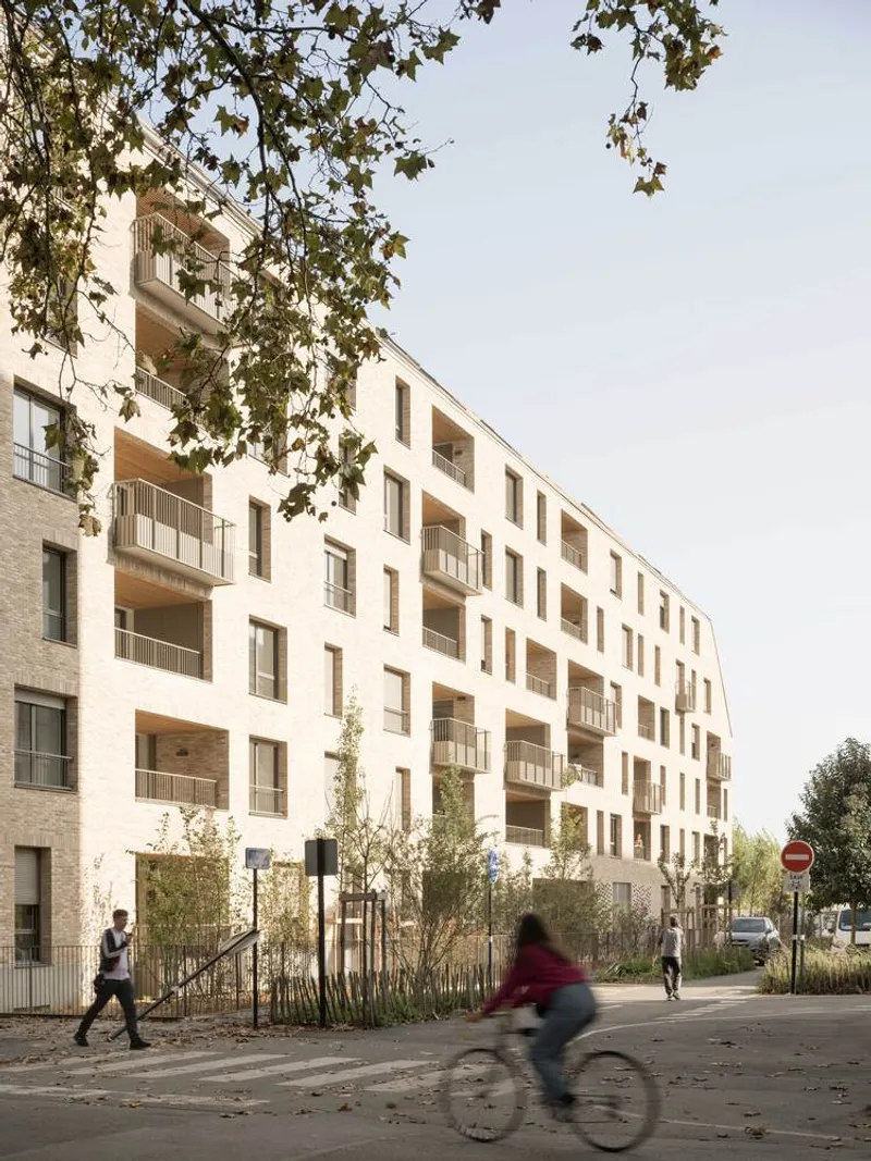 Street view of the residential facade with young trees and a cyclist passing by