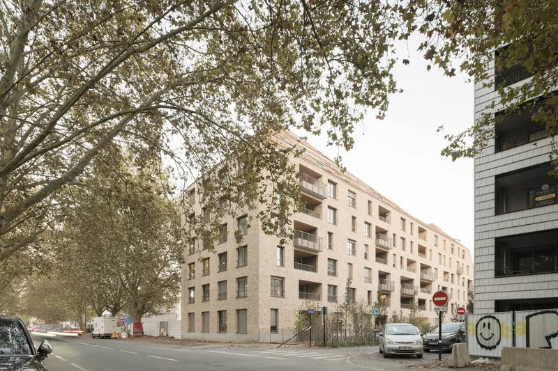 Street view of the pale brick facade through mature tree branches on an overcast day