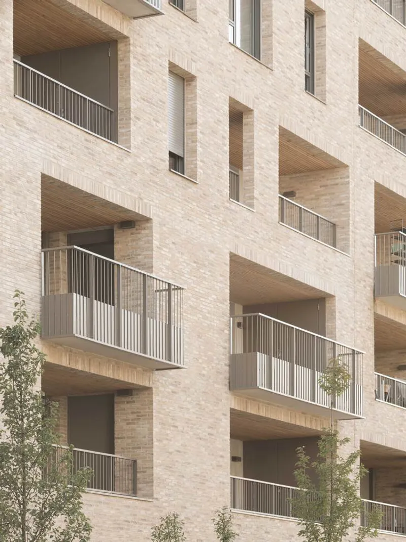 Staggered balconies with timber soffits and metal railings set into a pale brick facade with young trees