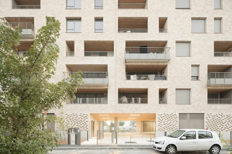 Ground-level entrance with perforated brick screen and recessed timber soffit beside a parked white car