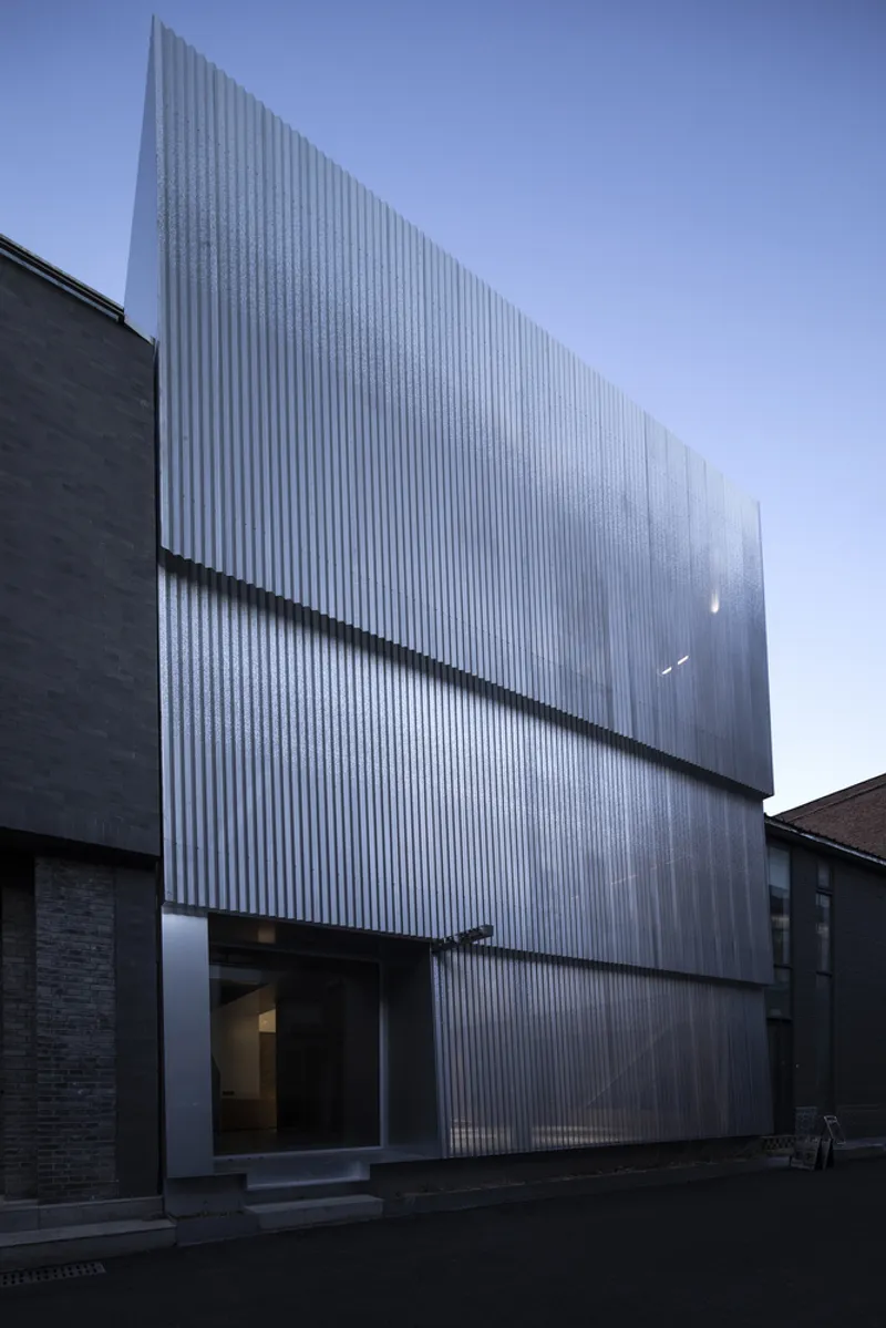 Vertical ribbed metal facade with horizontal recessed joints at dusk