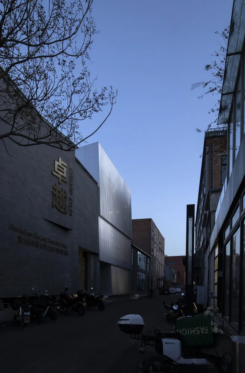 Street view of the ribbed metal volume among brick buildings with bare tree branches overhead