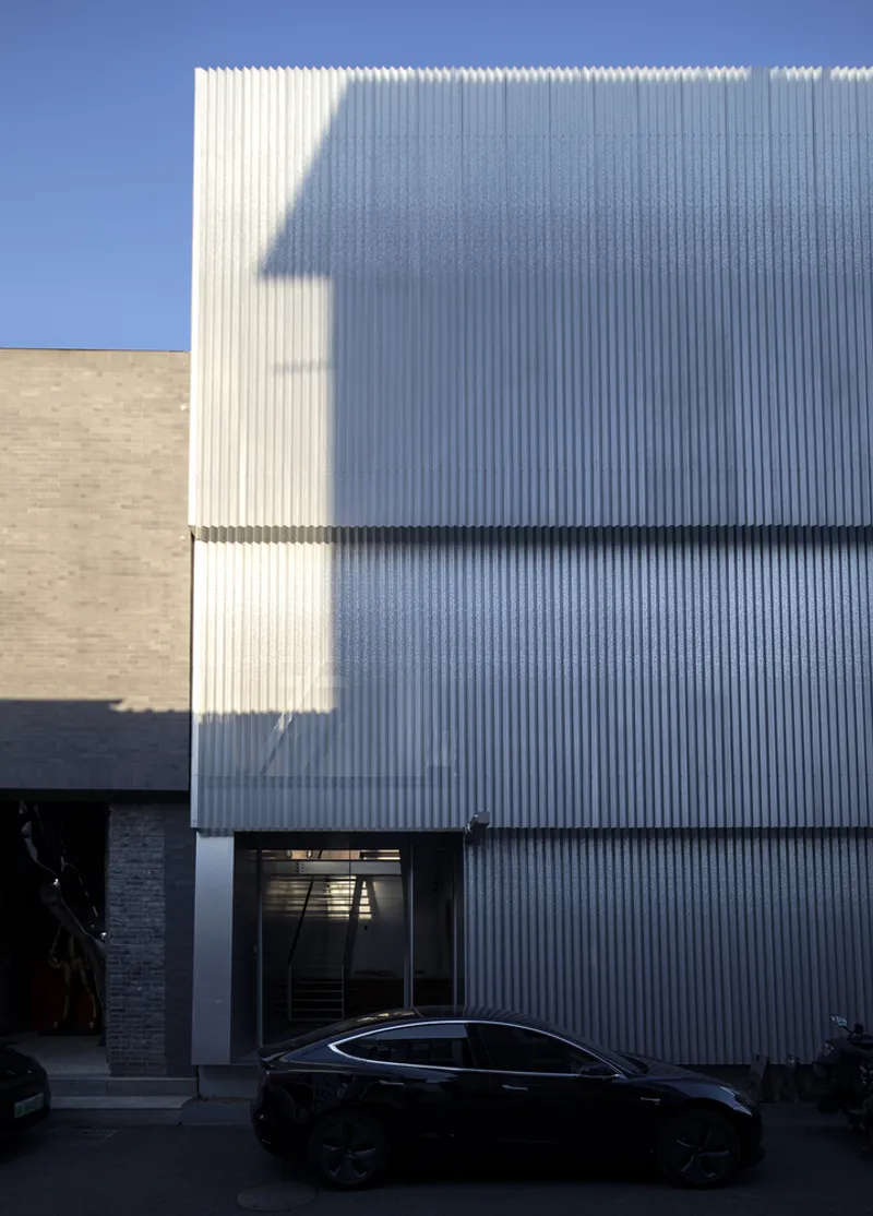 Vertical corrugated metal facade with staggered volumes casting shadows under a clear blue sky