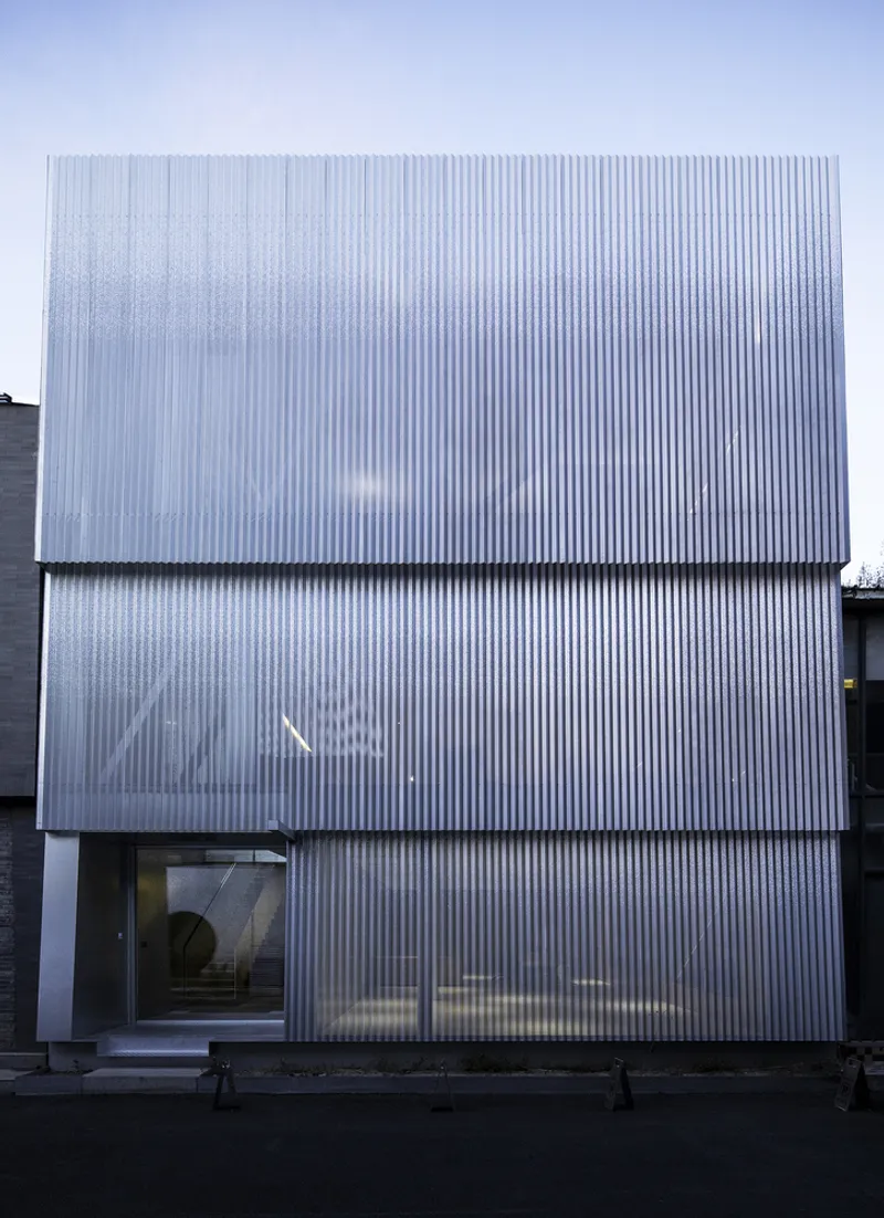 Head-on view of the ribbed metal facade with a single horizontal window slot at street level