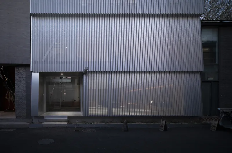 Street-level view of corrugated cladding with recessed entrance and glazed opening at dusk
