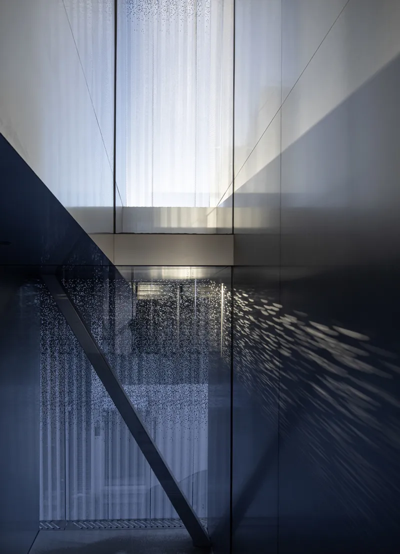 Double-height void with white curtains filtering daylight through glass bridge and perforated metal screen