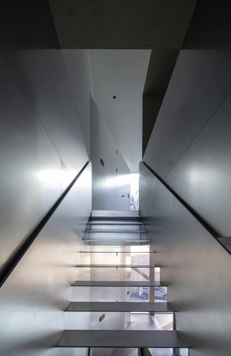 Steel staircase rising through a narrow white-walled shaft with black handrails and skylight above