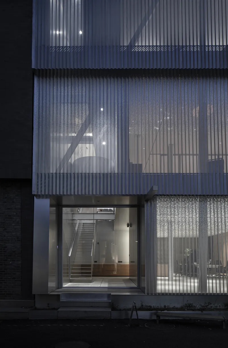 Night view of translucent corrugated walls with interior staircase visible through illuminated panels