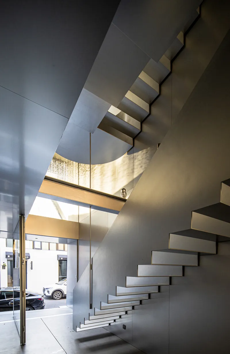 Double-height entrance hall with floating steel stair beneath a skylight and glazed door to the street