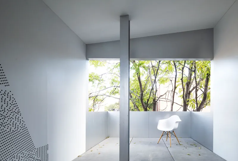 Upper-level courtyard terrace enclosed by half-height walls with trees visible beyond and a single chair