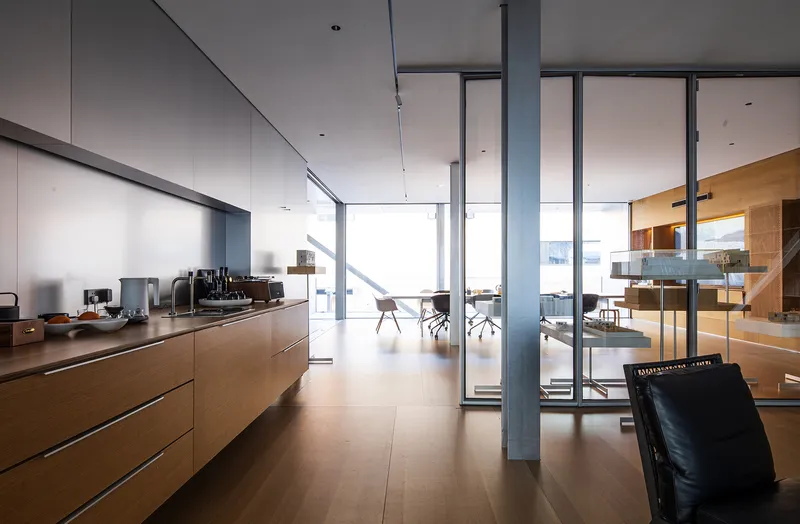 Open office interior with wood cabinetry and floor-to-ceiling glazing overlooking workspace beyond