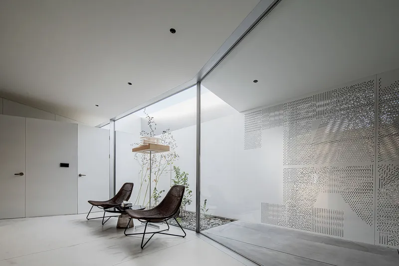 Interior courtyard with planted bed and perforated white metal screen filtering daylight