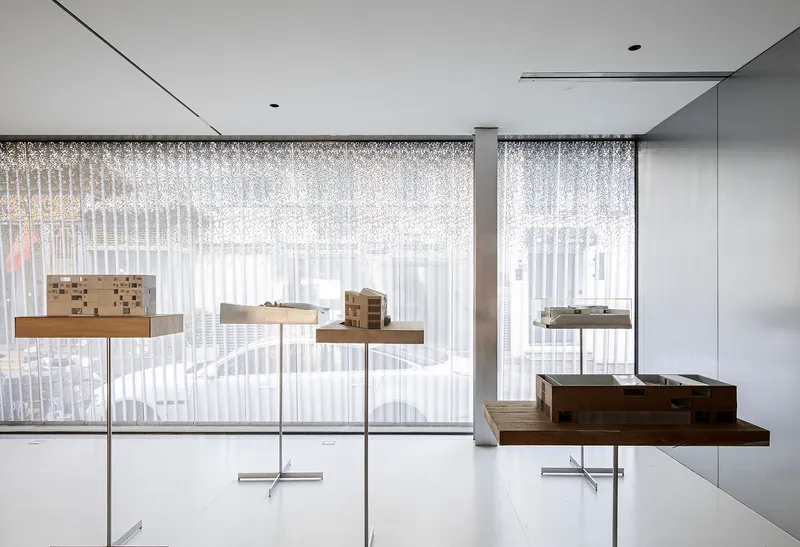 Architectural models displayed on pedestal stands behind sheer curtains and floor-to-ceiling windows
