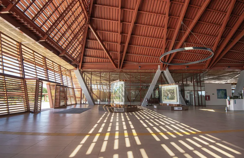 Interior concourse with exposed timber roof trusses casting diagonal shadows across the polished floor