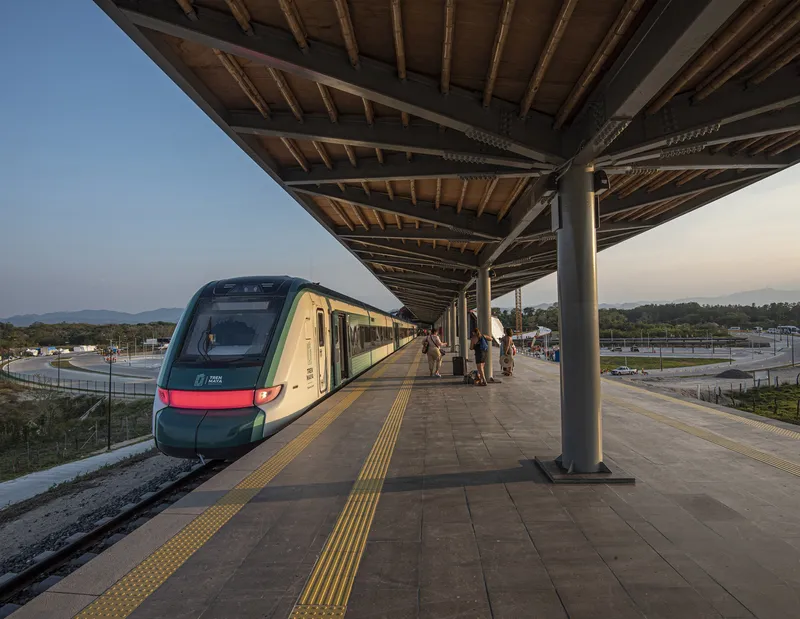 Train platform with exposed timber roof structure and steel columns at dusk with passengers waiting