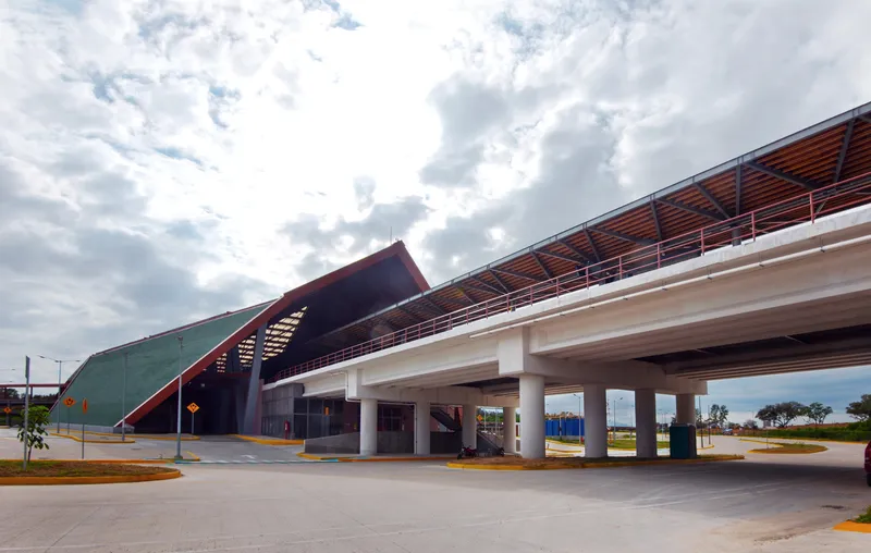 Elevated pedestrian bridge with timber louvered canopy and steel columns crossing a roadway under cloudy skies