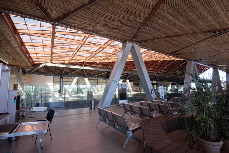 Waiting area with woven bamboo ceiling, white V-shaped columns, and potted plants beneath skylights