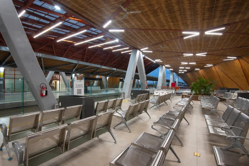Interior terminal hall with rows of metal seating, bamboo ceiling panels, and linear fluorescent fixtures