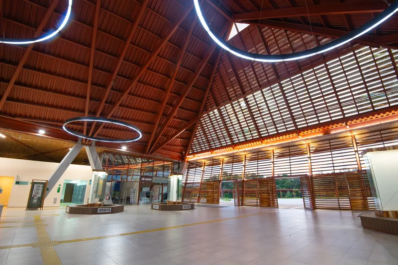 Terminal hall with timber slat screens, circular ring lighting, and angled V-columns below vaulted ceiling