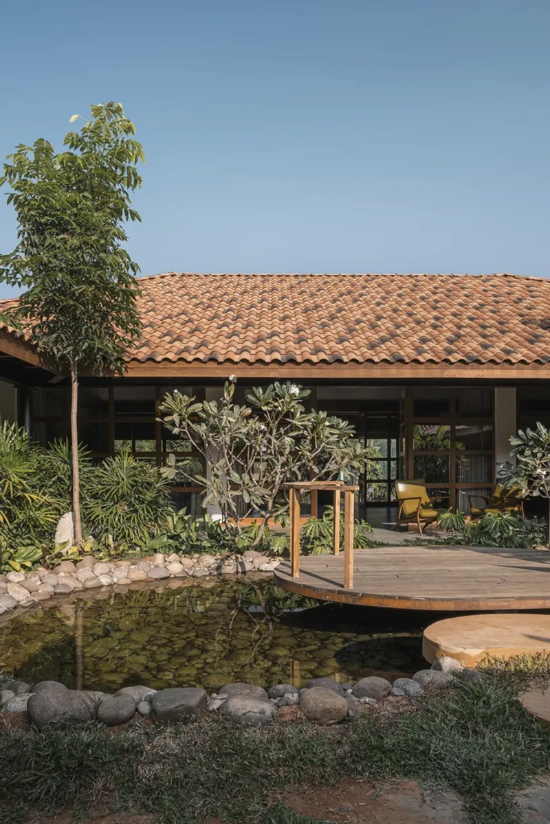 Clay tile roof over an open pavilion with planted pond and timber deck under afternoon light