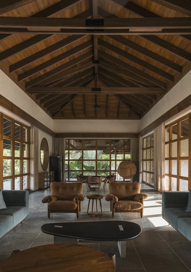 Living room with exposed timber truss ceiling and arched mirror above leather armchairs