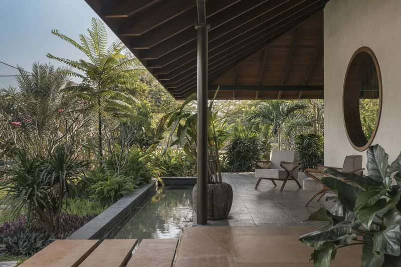 Covered terrace with exposed timber beams and steel column overlooking a reflecting pool and tropical garden