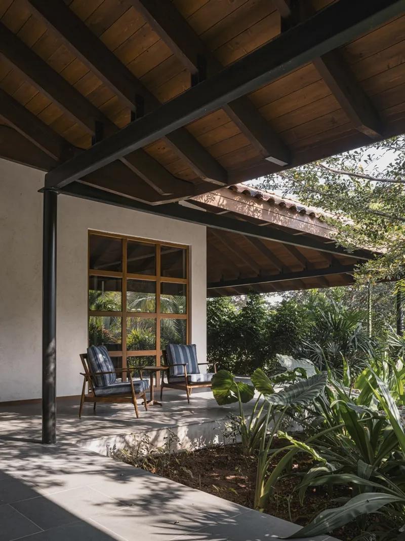 Shaded terrace with timber ceiling and steel columns framing planted beds and dappled sunlight