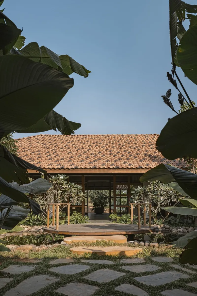 Open pavilion with clay tile roof framed by banana leaves and stone pathway in afternoon light