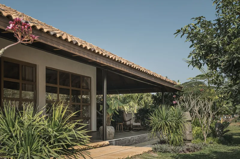 Covered terrace with timber columns and clay tile roof surrounded by succulent plantings and flowering trees
