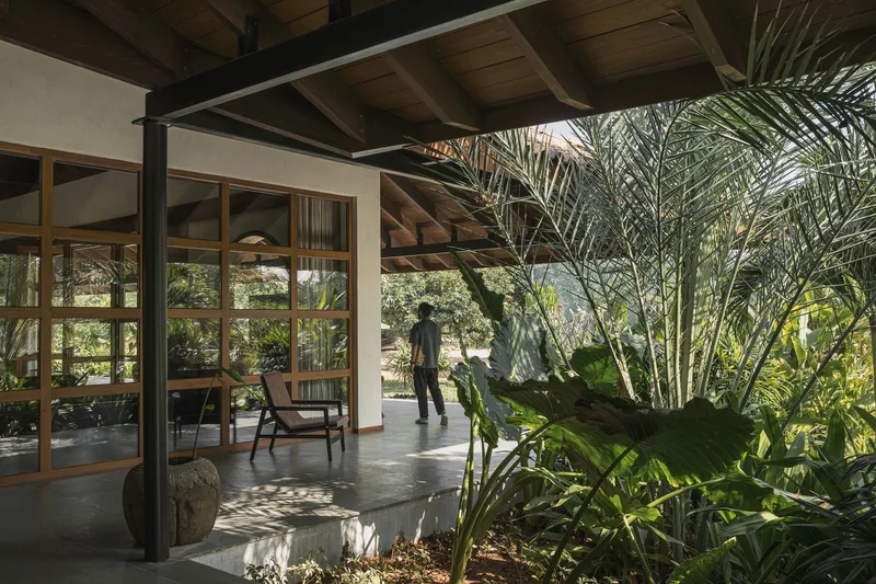 Covered porch with exposed timber ceiling and steel columns opening to a courtyard with palm fronds