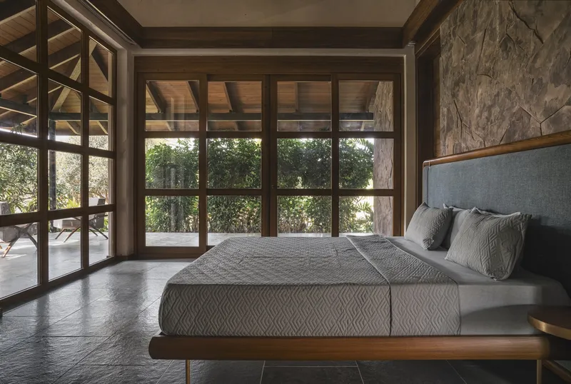 Bedroom with floor-to-ceiling gridded glass doors framing views of exterior vegetation and terrace