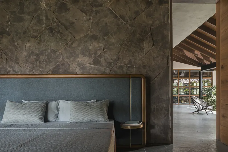 Bedroom corner showing dark stone wall panels meeting timber ceiling beams and doorway beyond