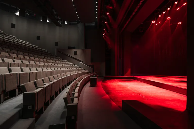 Theater auditorium with raked seating facing a stage washed in red lighting