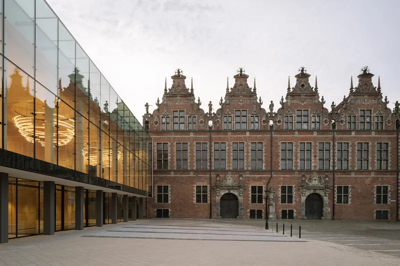Glass curtain wall extension facing the stepped brick facades of the existing structures across the plaza