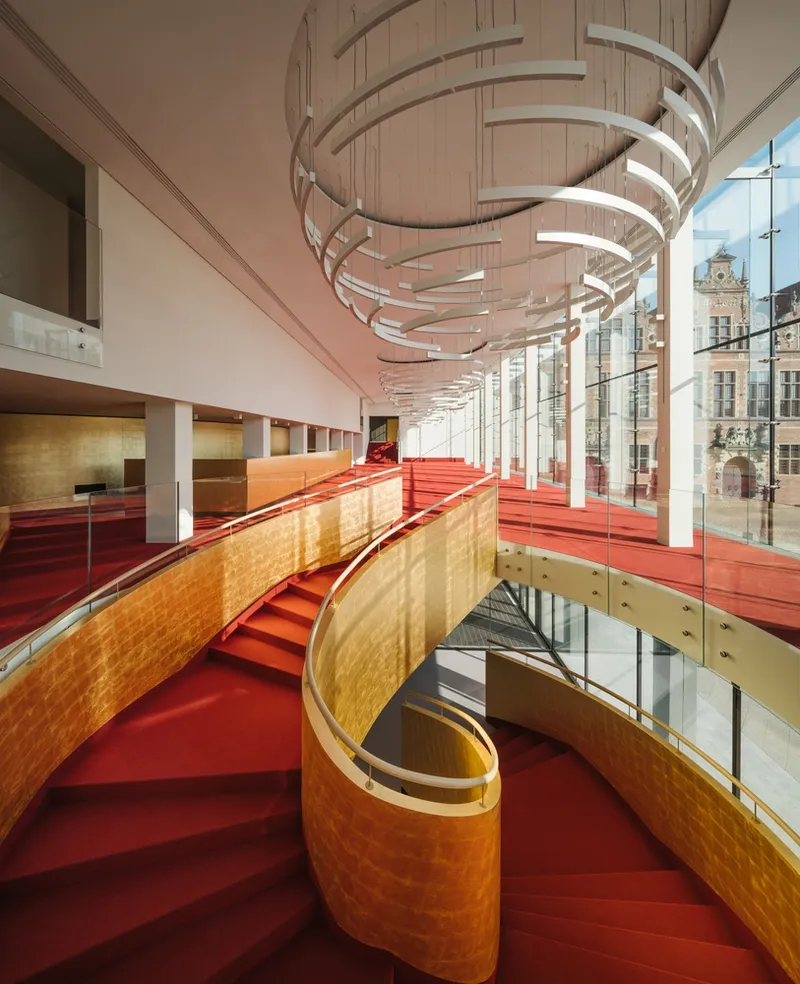 Red carpeted staircase with curved timber balustrades ascending beneath a spiraling sculptural light fixture