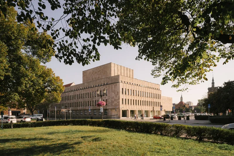 Tiered stone facade framed by mature trees along a park lawn in late afternoon light