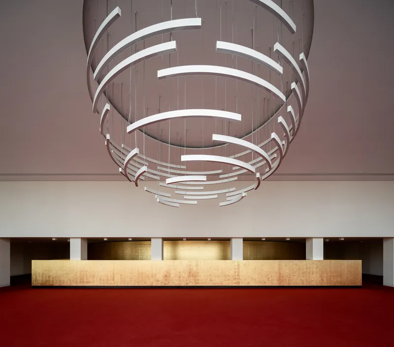 Lobby foyer with long timber reception desk beneath a spiraling light fixture over red carpet