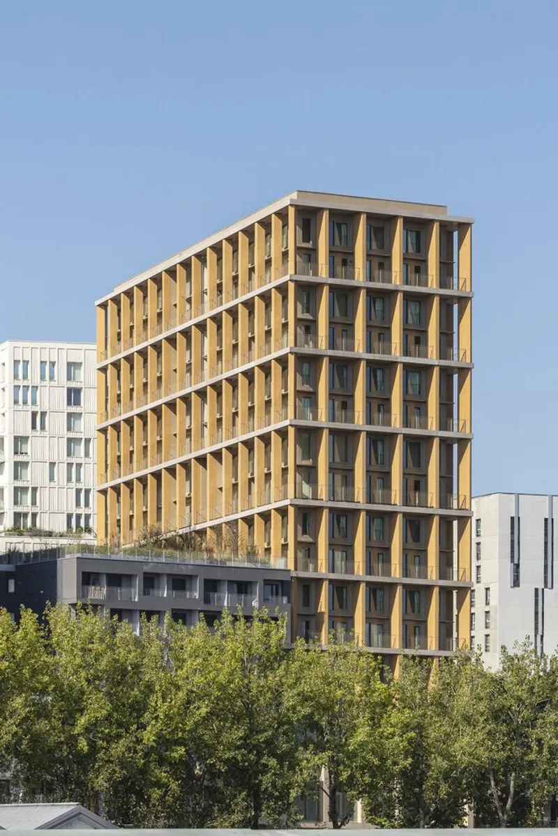 Facade with vertical timber brise-soleil framing the glazed openings above a row of young trees