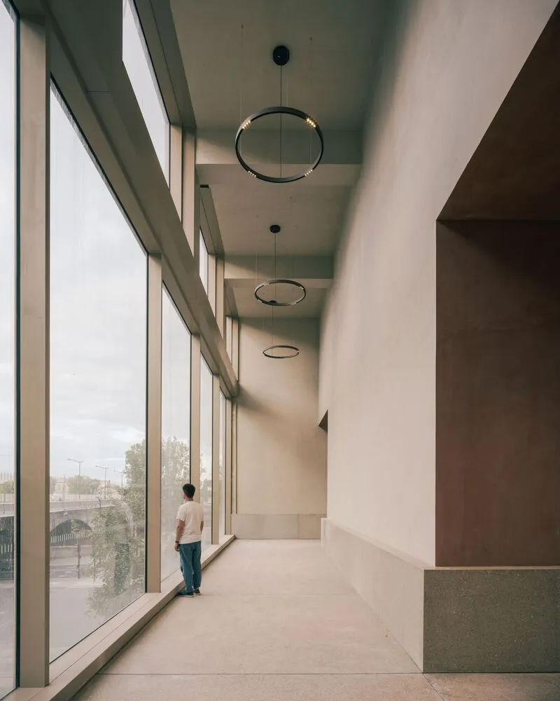 Corridor with full-height glazing and circular pendant lights where a person stands looking out