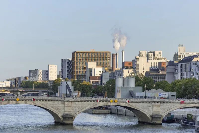 Distant view across the river showing the tower rising above the stone bridge and industrial skyline